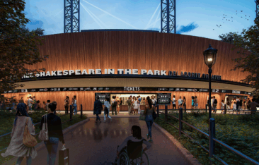 A crowd approaches the ticket area of the Delacorte Theater at dusk, with illuminated signage for Shakespeare in the Park and people entering, including a person using a wheelchair in the foreground.